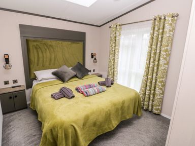 A bedroom with a large bed covered with green bedding two gray pillows and folded towels on top next to a window with patterned curtains at Ramsey in Broad Haven