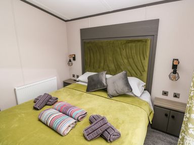 A bedroom with a green bedspread and pillows on the bed with folded towels on top at Ramsey in Broad Haven
