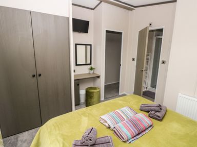 A bedroom with a bed with towels folded on it a wardrobe a dressing table with a mirror and a small green stool Ramsey Broad Haven