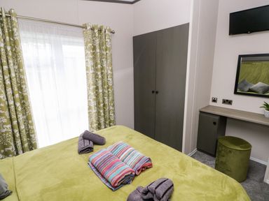A bedroom with a green bedspread folded towels a wardrobe a desk with a mirror a small stool and curtains at Ramsey in Broad Haven
