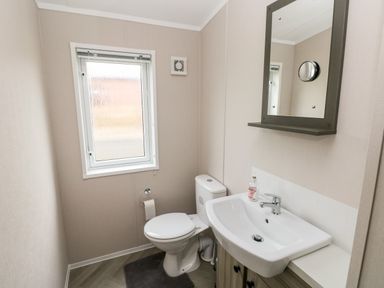 A bathroom with a toilet a sink with a cabinet mirror and a window at Ramsey in Broad Haven