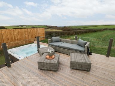 An outdoor deck with wicker sofa and tables overlooking fields and a hot tub at Ramsey in Broad Haven