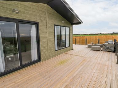 A wooden deck with outdoor seating and glass doors at Ramsey in Broad Haven