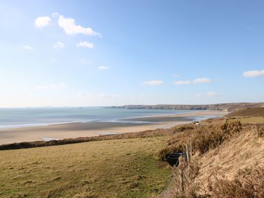 A coastal landscape with a sandy beach, grassy fields, and hills in the distance at Ramsey in Broad Haven