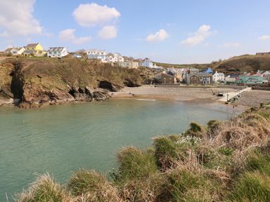A coastal village with houses on cliffs overlooking a small beach and calm water at Ramsey in Broad Haven