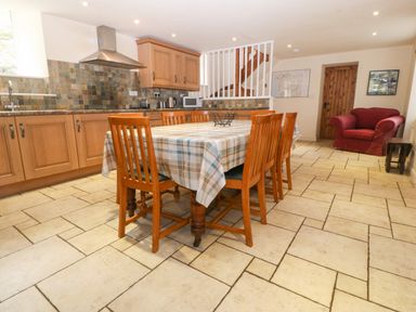 A kitchen dining area with a wooden table and six chairs a red armchair and wooden cabinets at Tyn Llwyn in Eisingrug near Harlech