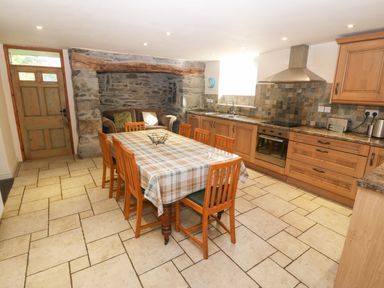 A kitchen with wooden cabinets a dining table with chairs and a stone wall at Tyn Llwyn in Eisingrug near Harlech