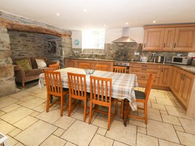 A kitchen with wooden cabinets dining table with chairs and a sofa in a stone alcove at Tyn Llwyn in Eisingrug near Harlech