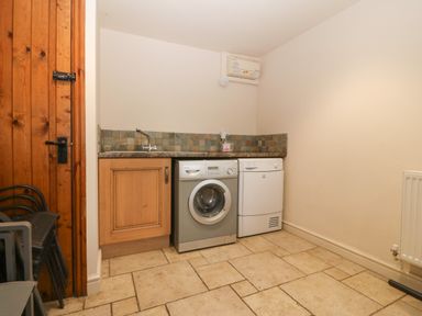 A utility room with a washing machine dryer sink and wooden door at Tyn Llwyn in Eisingrug near Harlech