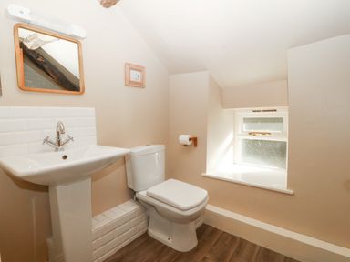 A bathroom with a pedestal sink a toilet a mirror a small window and wooden flooring at Tyn Llwyn in Eisingrug near Harlech
