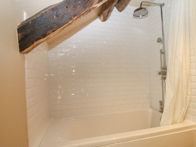 A bathroom with a bathtub shower curtain and exposed wooden beam at Tyn Llwyn in Eisingrug near Harlech