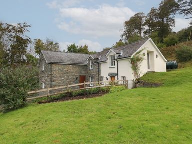 A house with stone and white walls surrounded by grass and trees at Tyn Llwyn in Eisingrug near Harlech