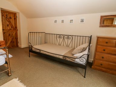 A bedroom with a metal framed single bed a wooden chest of drawers and a wooden door at Tyn Llwyn in Eisingrug near Harlech