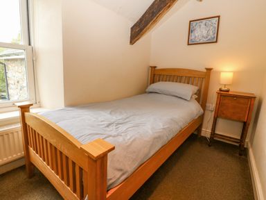A small bedroom with a single wooden bed next to a window and a wooden nightstand with a lamp at Tyn Llwyn in Eisingrug near Harlech