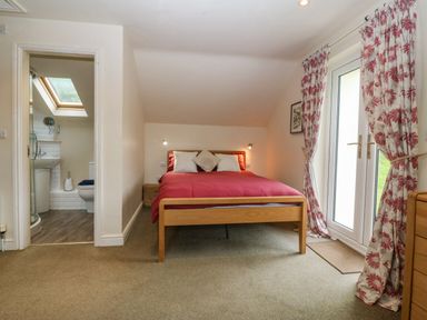 A bedroom with a double bed red bedding bedside table and door leading to an en suite bathroom at Tyn Llwyn in Eisingrug near Harlech