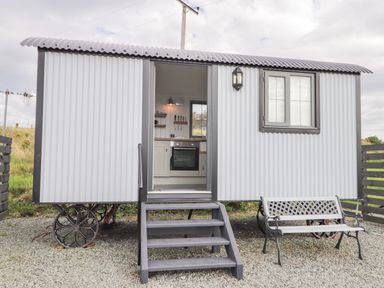 An exterior view of a small corrugated metal hut on wheels with steps leading to an open door and a bench nearby at Shepherds Hut in Dunvegan