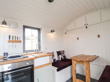 A small kitchen and dining area with a stove sink wooden table and cushioned benches at Shepherds Hut in Dunvegan