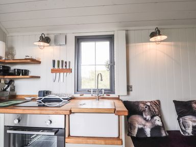 A kitchen with a window sink stove and knives on a magnetic strip with cushions on a bench at Shepherds Hut in Dunvegan