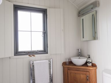 A bathroom with a window above a towel rack with a white towel a wooden vanity with a white sink a glass and soap dispenser and a mirror above at Shepherds Hut in Dunvegan