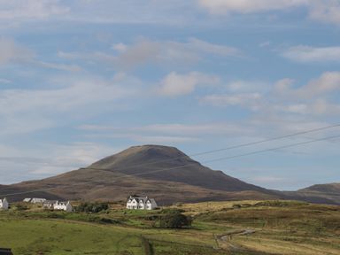 A rural landscape with green fields a winding road white houses and a mountain in the background at Shepherds Hut in Dunvegan