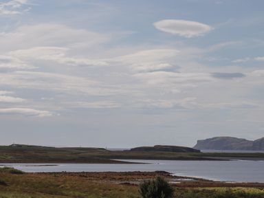 A coastal landscape with water, grassy land, and cliffs in the distance at Shepherds Hut in Dunvegan