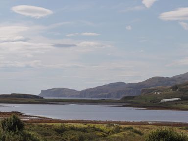 A landscape with a body of water in the foreground and hills in the background at Shepherds Hut in Dunvegan