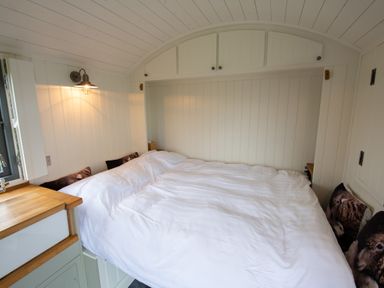 A small bedroom with a white bed and wooden cabinets overhead in Shepherds Hut Dunvegan