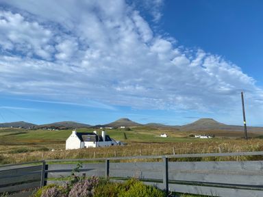 A rural landscape with white houses green fields hills and a blue sky at Shepherds Hut in Dunvegan