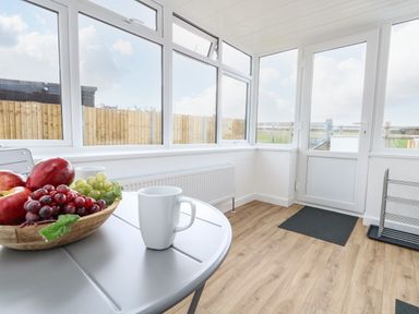 A room with large windows wooden floor a table with a bowl of fruit and two white mugs at Cliff Barn in Burton Bradstock