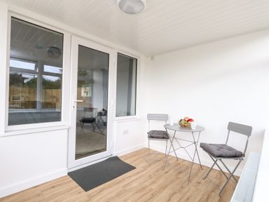 A small indoor seating area with two chairs and a round table with fruit bowl near a glass door at Cliff Barn in Burton Bradstock