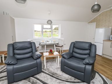 A living room with two black armchairs a small table with fruit a dining table with chairs and a kitchen area at Cliff Barn in Burton Bradstock