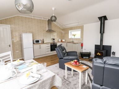 An open plan kitchen and living area with dining table fridge stove armchairs and a wood burning stove at Cliff Barn Burton Bradstock