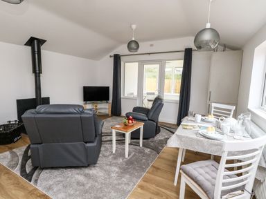 A living room with two armchairs a small table with fruit a dining table set for two and a television at Cliff Barn in Burton Bradstock