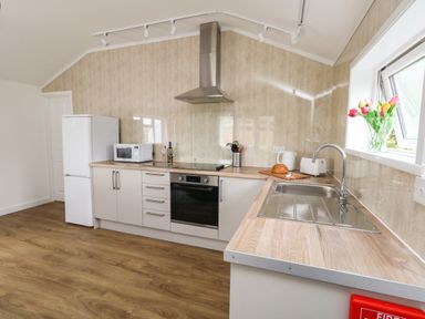 A kitchen with white cabinets a refrigerator a microwave an oven a cooktop a sink and flowers on the windowsill at Cliff Barn in Burton Bradstock