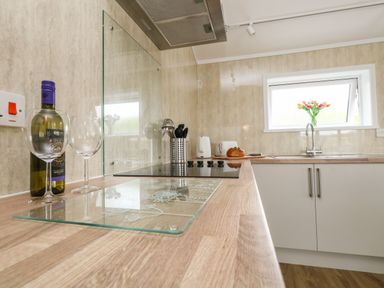 A kitchen countertop with a bottle of wine and two wine glasses a stove cooking utensils a loaf of bread a kettle a toaster and a window with flowers at Cliff Barn in Burton Bradstock