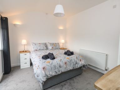 A bedroom with a double bed floral bedding bedside tables with lamps and rolled towels at Cliff Barn in Burton Bradstock