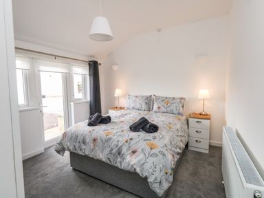 A bedroom with a double bed floral bedding bedside tables with lamps and a glass door at Cliff Barn in Burton Bradstock