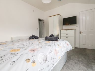A bedroom with a bed with floral bedding folded towels a white wardrobe a chest of drawers and a wall-mounted TV at Cliff Barn in Burton Bradstock
