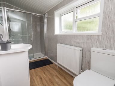 A bathroom with a shower enclosure a toilet a radiator a sink and a window at Cliff Barn in Burton Bradstock