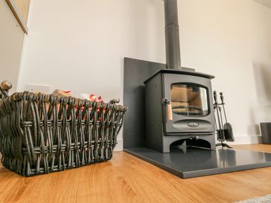 A wood stove with fireplace tools and a wicker basket on a wooden floor at Cliff Barn in Burton Bradstock
