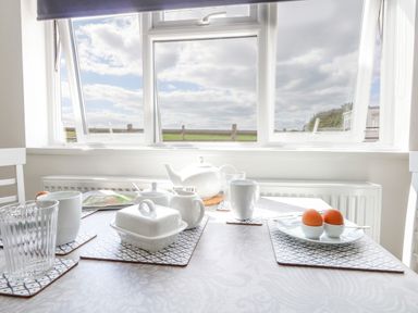 A dining table set with cups teapot plates and boiled eggs by a window at Cliff Barn in Burton Bradstock
