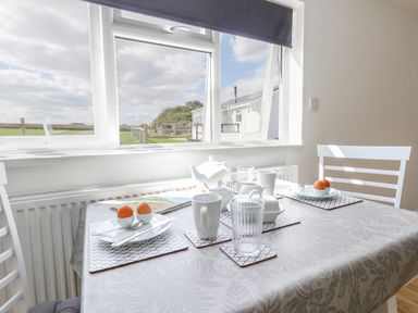A dining table set with cups, glasses, teapot, and soft-boiled eggs near a window with a view of a green field at Cliff Barn Burton Bradstock