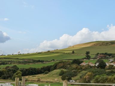 Green hills with scattered houses and trees under a blue sky at Cliff Barn in Burton Bradstock