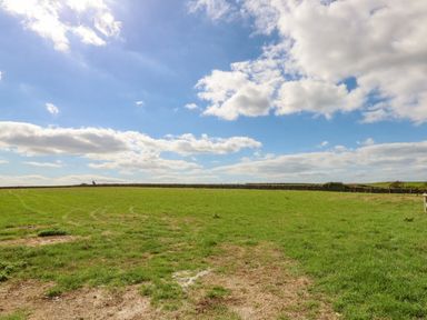A green grassy field under a blue sky with scattered clouds at Cliff Barn in Burton Bradstock