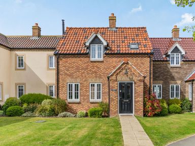 A brick house with a tiled roof a black front door and windows with white frames and a garden path at Lantern House in Filey