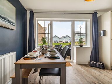 A dining area with a wooden table set for four people near sliding glass doors showing outdoor seating at Lantern House in Filey