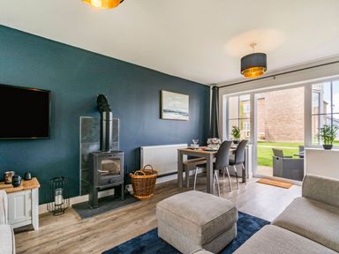 A living room with a wood stove dining table chairs and glass doors opening to a garden at Lantern House in Filey