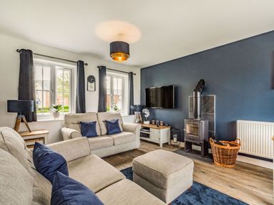 A living room with beige sofas navy cushions wood burning stove and wall mounted television at Lantern House in Filey