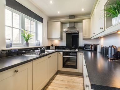 A kitchen with cabinets a stove oven microwave toaster and windows at Lantern House in Filey