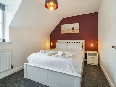 A bedroom with a double bed and folded towels on it two bedside tables with lamps and a window at Lantern House in Filey